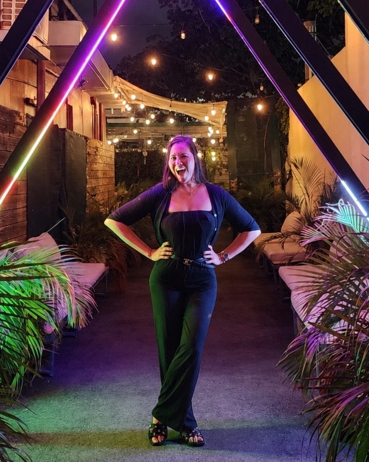 Michelle smiling with her hands on her hips in a lit-up courtyard at night